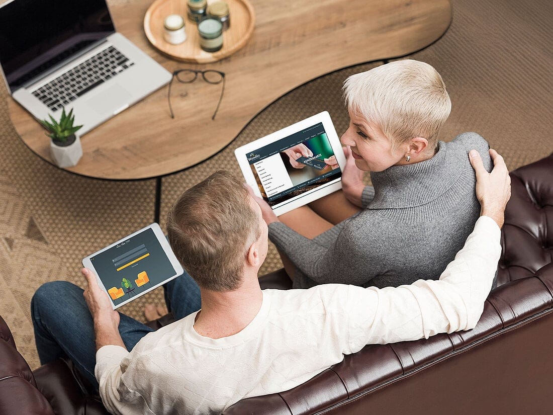 Paar auf dem Sofa bespricht mit Tablets die Einrichtungsplanung