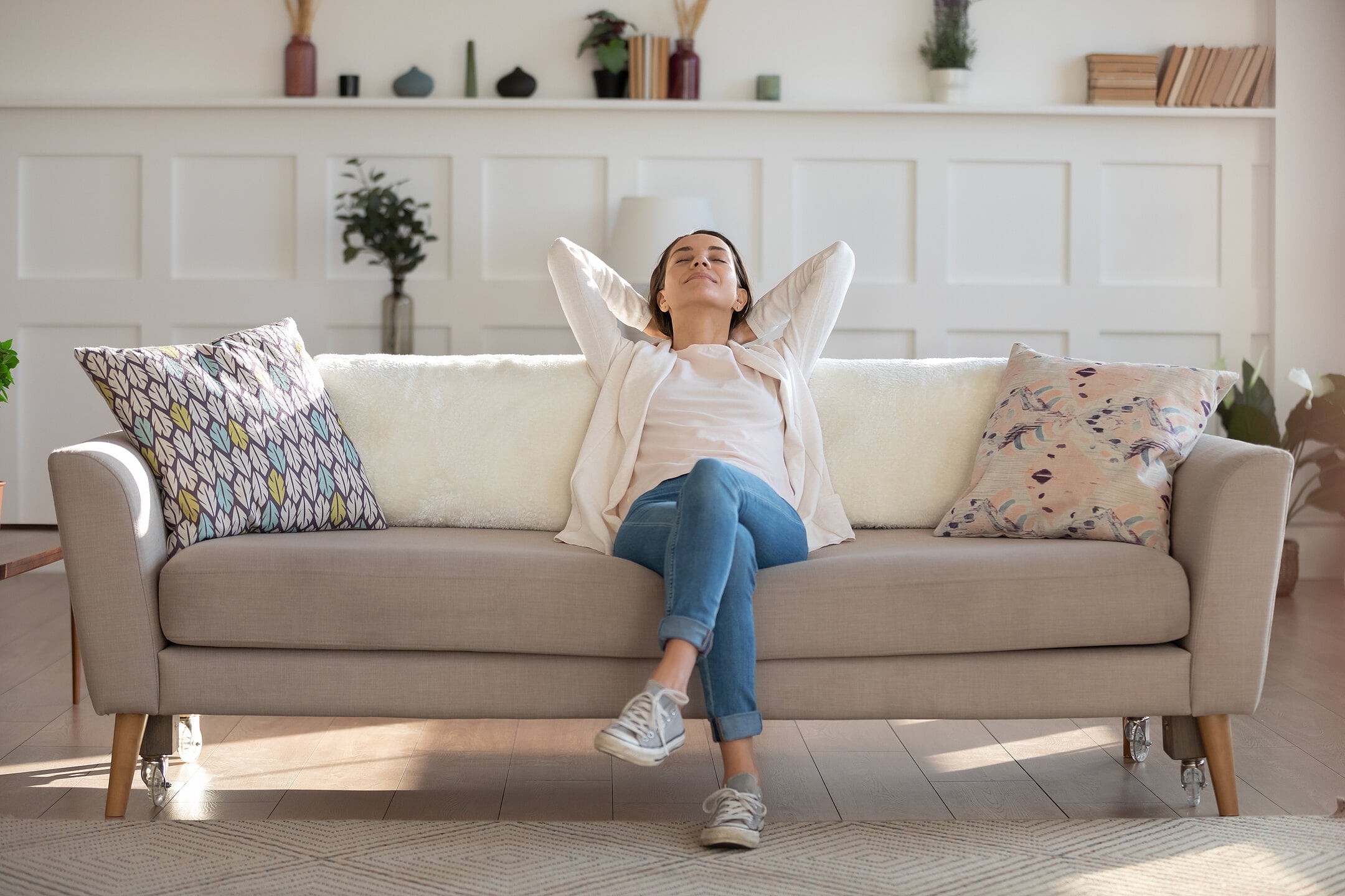 Frau lehnt sich entspannt auf einem hellen Sofa in ihrem Wohnzimmer zurück